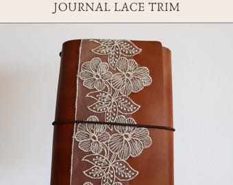 May include: A brown leather journal featuring a vertical strip of white floral lace trim attached to the cover. The text Add-On JOURNAL LACE TRIM is printed at the top. A thin black elastic band wraps horizontally around the center of the journal.