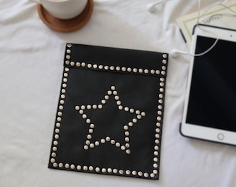 May include: A black rectangular pouch featuring a star-shaped pattern outlined with silver-toned metal studs. The pouch has a fold-over flap design, with additional silver studs lining the entire perimeter of the front panel and the flap edge.