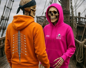 May include: Two figures with skull faces stand on a wooden deck, wearing orange and pink hoodies. The orange hoodie features a white rowing graphic on the back. The pink hoodie has a skull and crossbones logo with the text "Skull & Team".