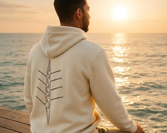 May include: Cream-colored hoodie with a rowing design on the back. The hoodie features a graphic of a rowing shell and oars. The word "ROWING" is printed above the logo. The text "Suivez la ligne..." is at the bottom.