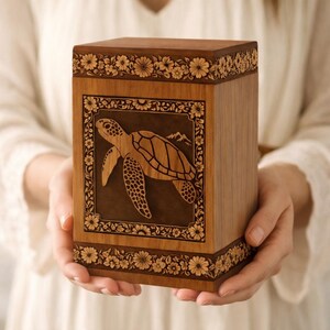 May include: A wooden urn with a detailed turtle carving on the front. The urn is rectangular with floral carvings around the top and bottom. The turtle is surrounded by a decorative border and mountain scene.