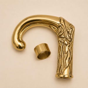 Può includere: Un manico per bastone in metallo color oro lucido con una parte superiore curva e un design botanico in rilievo testurizzato sull'asta verticale. Un anello cilindrico liscio in metallo color oro è posizionato accanto al manico.