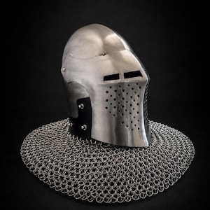 Puede incluir: Un casco de bacinete de acero pulido con una cúpula redondeada, una visera puntiaguda con ranuras oculares horizontales y una placa frontal perforada. Un almete de cota de malla plateada está unido a la base, extendiéndose en círculo.
