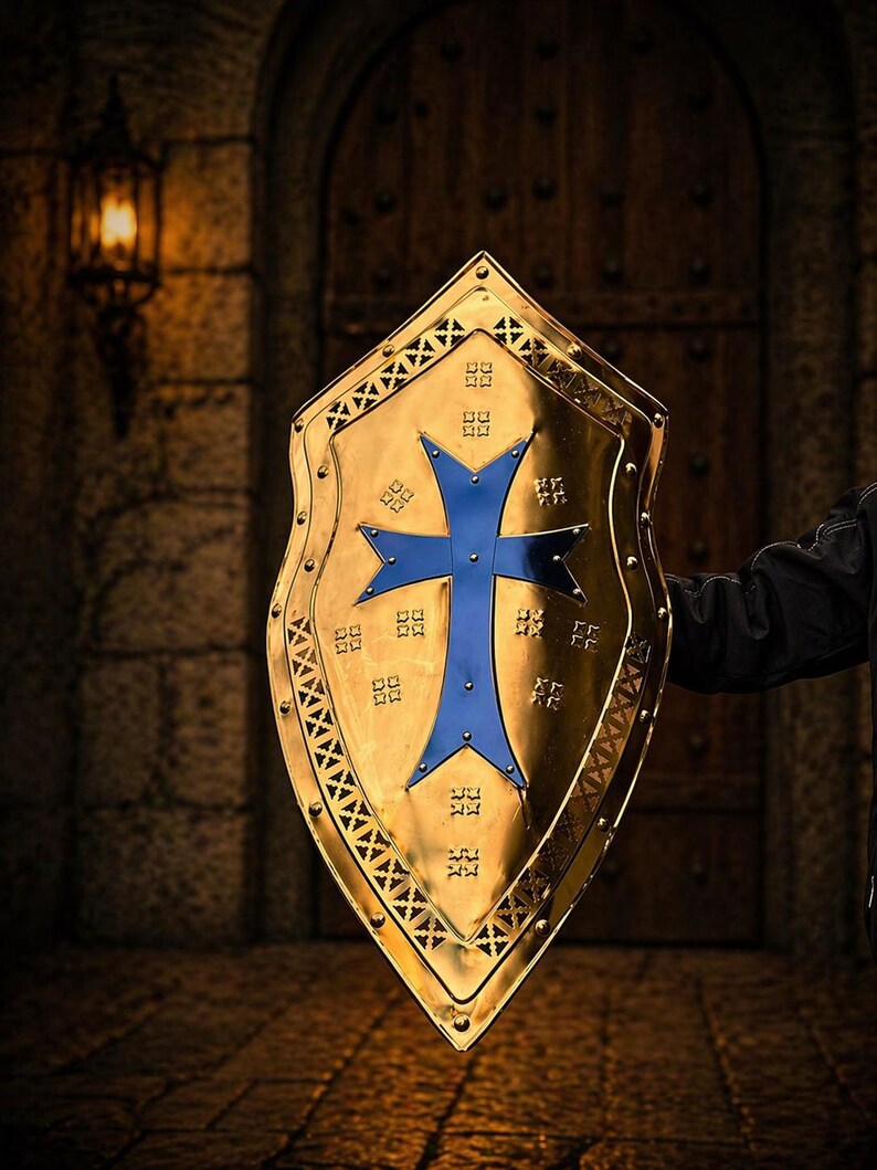 Op de afbeelding: Een goudkleurig schild met een blauw kruisontwerp. Het schild heeft een decoratieve rand en wordt gehouden tegen een vage achtergrond van een stenen muur en houten deur.