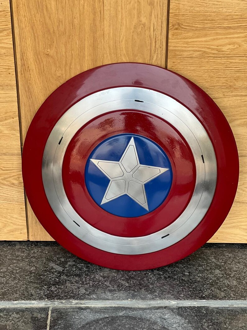 K&ouml;nnte beinhalten: Ein runder Schild im Captain America-Design. Er hat einen roten Au&szlig;enring, einen silbernen Ring und eine blaue Mitte mit einem wei&szlig;en Stern. Der Schild ist eine Nachbildung.