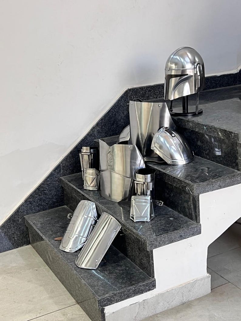 May include: A collection of shiny, silver-colored armor pieces, including a helmet, chest plate, and various limb guards, arranged on a set of granite stairs. The armor appears to be made of metal and is likely for cosplay or display.