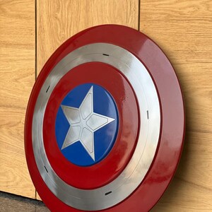 K&ouml;nnte beinhalten: Ein runder Schild mit einem roten Au&szlig;enring, einem silbernen Innenring und einer blauen Mitte. Ein wei&szlig;er Stern befindet sich in der Mitte des blauen Kreises. Der Schild ist eine Nachbildung von Captain Americas Schild.