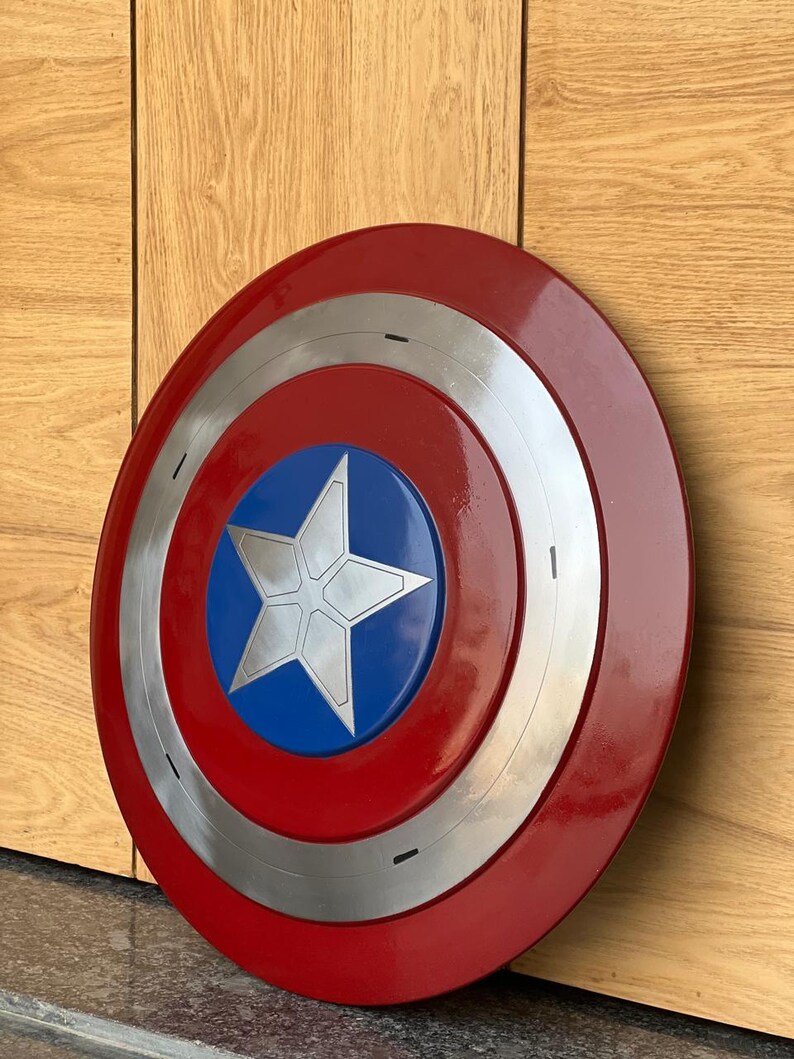 K&ouml;nnte beinhalten: Ein runder Schild mit einem roten Au&szlig;enring, einem silbernen Innenring und einer blauen Mitte. Ein wei&szlig;er Stern befindet sich in der Mitte des blauen Kreises. Der Schild ist eine Nachbildung von Captain Americas Schild.