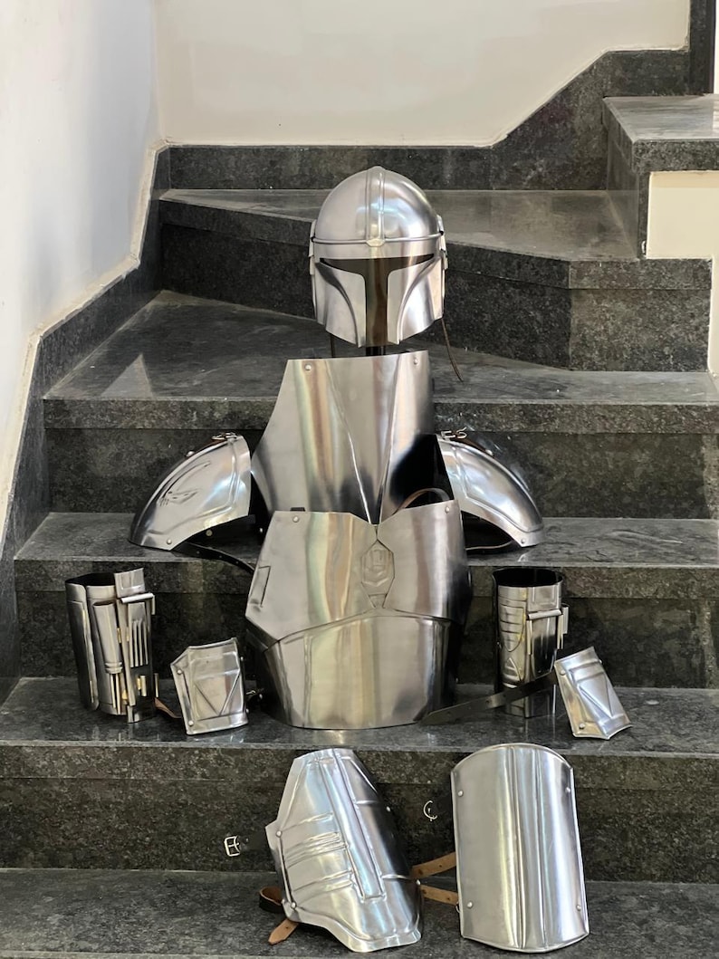 May include: A complete set of silver-colored Mandalorian armor, including a helmet, chest plate, shoulder pads, and various leg and arm pieces. The armor is displayed on a set of stairs.