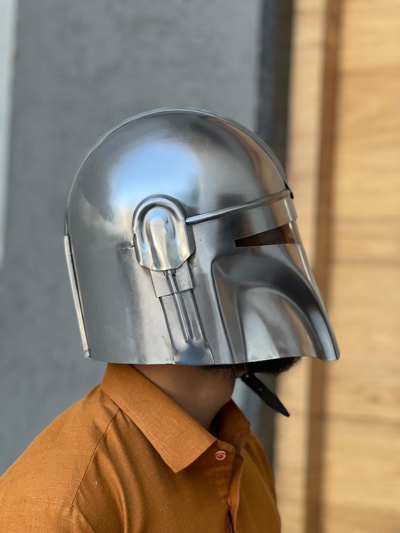 May include: A polished silver helmet with a visor and a curved design. The helmet has a smooth, reflective surface, likely made of metal. It is a costume piece, possibly for cosplay or a themed event.