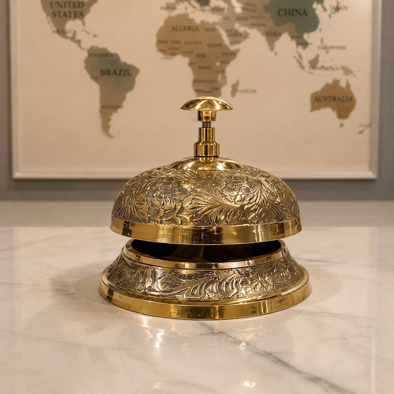 Peut inclure: Une cloche de service en laiton poli orn&eacute;e d'une gravure florale complexe sur son d&ocirc;me et sa base. La cloche pr&eacute;sente un m&eacute;canisme &agrave; bouton-poussoir central et une forme circulaire, avec une finition dor&eacute;e m&eacute;tallique et des motifs en relief.