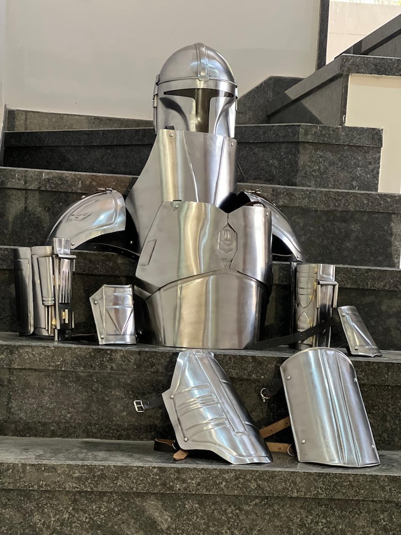 May include: A complete set of polished silver armor, including a helmet, chest plate, shoulder guards, and leg armor. The armor is displayed on a set of stairs, showcasing its intricate design and metallic sheen. This set is reminiscent of a sci-fi or fantasy theme.
