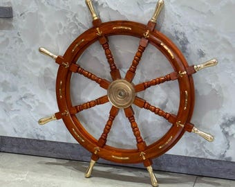 May include: A wooden ship's wheel featuring a polished brass centre hub and eight brass handles. The circular frame is constructed from dark brown wood with brass anchor-shaped inlays positioned between each of the eight spokes.