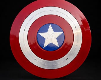Puede incluir: Un escudo circular que presenta un anillo exterior rojo brillante, un anillo central de plata cepillada y un círculo azul en el centro que contiene una prominente estrella plateada de cinco puntas. El diseño es simétrico con un acabado liso y reflectante.