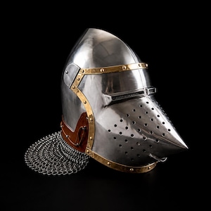 May include: A polished steel bascinet helmet featuring a pointed visor with ventilation holes, brass trim accents, and a brown leather band. A silver-toned chainmail aventail is attached to the base of the helmet, providing neck protection.