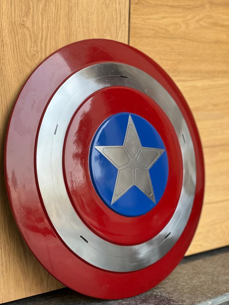 K&ouml;nnte beinhalten: Runder Schild im Captain America-Stil mit einem roten Au&szlig;enring, einem silbernen Innenring und einer blauen Mitte mit einem silbernen Stern. Der Schild ist &uuml;berwiegend rot, silber und blau.