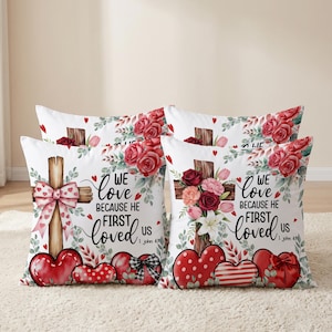 Könnte beinhalten: Vier quadratische Dekokissen mit weißem Hintergrund, einer Holzkreuz-Grafik, roten Rosen und Herzen. Der Text lautet: "WE love BECAUSE HE FIRST loved US 1 John 4:19". Die Designs zeigen rosa Schleifen, Punkte und Streifenmuster auf den Herzen.