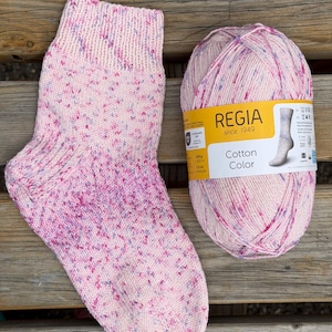 May include: A hand-knitted sock and a matching ball of yarn, both featuring a light pink base with speckled flecks of magenta and blue. The yarn label reads REGIA since 1949 Cotton Color, indicating a weight of 100 grams and 420 metres.