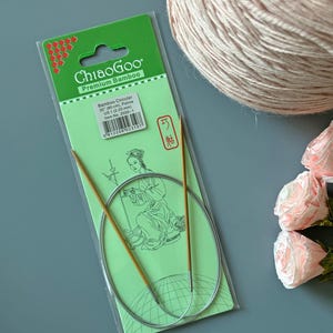 May include: ChiaoGoo Premium Bamboo circular knitting needles in packaging. The label specifies 32 inches (80 cm) and US 1 (2.25 mm). The packaging features a green background with a line drawing of a person and a barcode. The needles are light brown.