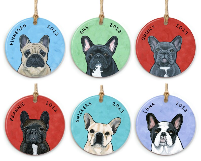 May include: Six round ceramic ornaments featuring French Bulldog portraits. Each ornament has a different dog breed and name, including Finnigan, Gus, Quincy, Frannie, Snickers, and Luna. The ornaments are decorated with a light blue, green, red, or purple background and the year 2023.