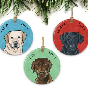 Puede incluir: Tres adornos navide&ntilde;os redondos de cer&aacute;mica con perros Labrador Retriever. Los adornos est&aacute;n decorados con el nombre del perro y el a&ntilde;o 2023. Los perros son un Labrador amarillo, un Labrador negro y un Labrador chocolate.