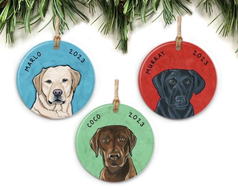Puede incluir: Tres adornos navide&ntilde;os redondos de cer&aacute;mica con perros Labrador Retriever. Los adornos est&aacute;n decorados con el nombre del perro y el a&ntilde;o 2023. Los perros son un Labrador amarillo, un Labrador negro y un Labrador chocolate.