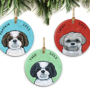 May include: Three round ceramic Christmas ornaments featuring Shih Tzu dogs. Each ornament has a different colored background: blue, red, and green. The dogs are painted in realistic detail. The ornaments are personalized with the names "Pumpkin", "Lucky", and "Theo" and the year "2023".