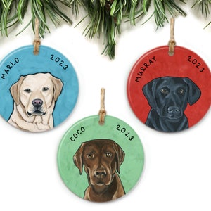 May include: Three round ceramic Christmas ornaments featuring Labrador Retriever dogs. The ornaments are decorated with the dog's name and the year 2023. The dogs are a yellow Labrador, a black Labrador, and a chocolate Labrador.