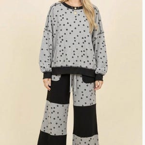 Könnte beinhalten: Ein Set aus einem grauen Langarm-Sweatshirt und einer weiten Hose mit einem sich wiederholenden schwarzen Blumenmuster. Das Sweatshirt hat einen schwarzen Rundhalsausschnitt und Bündchen. Die Hose zeigt ein Color-Block-Design mit abwechselnden Paneelen.