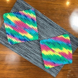 May include: Two colorful crocheted pot holders in a diamond shape. The pot holders are made with a multi-colored yarn with shades of pink, blue, green, and yellow.