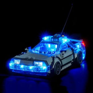 以下が含まれることがあります： 青色のLEDライトが外観を照らす、詳細なモデルカー。車はシルバーとグレーで、黒いホイールと長いアンテナが付いています。ライトは黒い背景に対して未来的な効果を生み出しています。