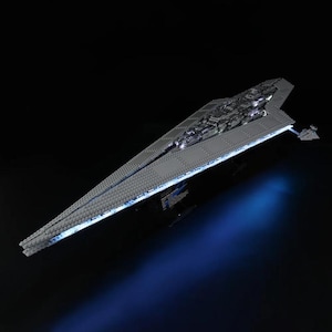Puede incluir: Maqueta gris de una nave espacial Star Destroyer, iluminada con luces azules y blancas sobre un fondo negro. El modelo es muy detallado, con intrincadas características de la superficie y una forma triangular alargada.