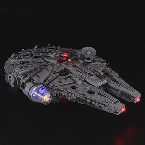 Könnte beinhalten: Ein detailliertes Modell des Raumschiffs Millennium Falcon, das aus ineinandergreifenden Blöcken besteht. Das graue Raumschiff verfügt über mehrere Fächer, eine Radarantenne und beleuchtete Lichter in Blau und Rot. Das Modell ist vor schwarzem Hintergrund.