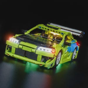 Op de afbeelding: Een limoengroene en zwarte speelgoedauto met een grote achterspoiler en witte koplampen. De auto heeft blauwe en groene accenten aan de zijkant en wordt verlicht met groene en oranje lichten, wat hem een futuristische uitstraling geeft.
