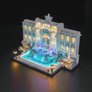 May include: A detailed miniature model of the Trevi Fountain, lit with warm and cool lights. The model shows intricate architectural details, a central arch, and a cascading water feature. The dark base provides a contrast to the bright structure.