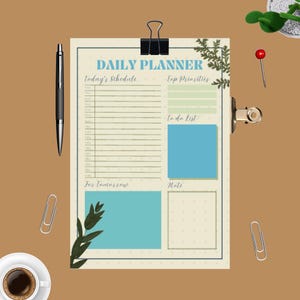 Puede incluir: Un planificador diario beige con un borde azul, sujeto por un clip negro. El planificador incluye secciones para el horario, las prioridades, la lista de tareas y las notas. También se ven un bolígrafo negro, clips y una taza de café.