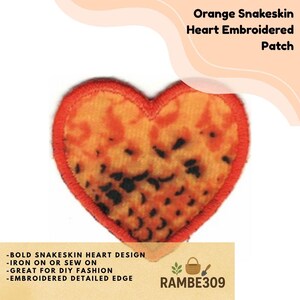 May include: Orange snakeskin heart embroidered patch. The patch features a heart shape with an orange and black snakeskin pattern and a red embroidered border. The text "Orange Snakeskin Heart Embroidered Patch" is at the top.