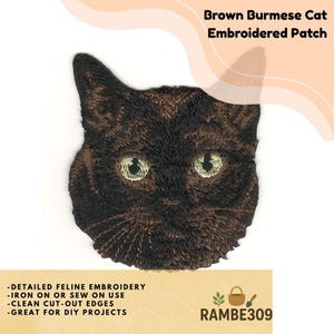 May include: Brown Burmese cat embroidered patch. The patch features a detailed embroidered design of a cat's face with green eyes and brown fur. The patch is suitable for DIY projects and can be ironed on or sewn on. The text "RAMBE309" is visible.