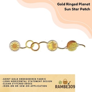 May include: Gold embroidered patch featuring a sun, star, and planet design. The patch has a long, horizontal design with clean stitched edges. The text on the patch reads "Gold Ringed Planet Sun Star Patch". The patch is iron-on or sew-on.