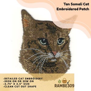 May include: Tan Somali cat embroidered patch. The patch features a detailed embroidered image of a cat's face with green eyes, tan fur, and white whiskers. The patch measures 2.75" x 2.5" and is iron-on or sew-on. The text "Tan Somali Cat Embroidered Patch" is visible.