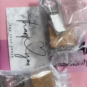 May include: A white card with marble pattern and black text reading Thank You FOR YOUR ORDER, accompanied by two small wooden mallets and a metal ring clip, each individually packaged in sheer white organza drawstring gift bags.