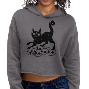 Gruselige süße Katze auf Haufen Schädel Fleece Crop Hoodie, Halloween Hexe Goth Cropped Sweatshirt mit Kapuze