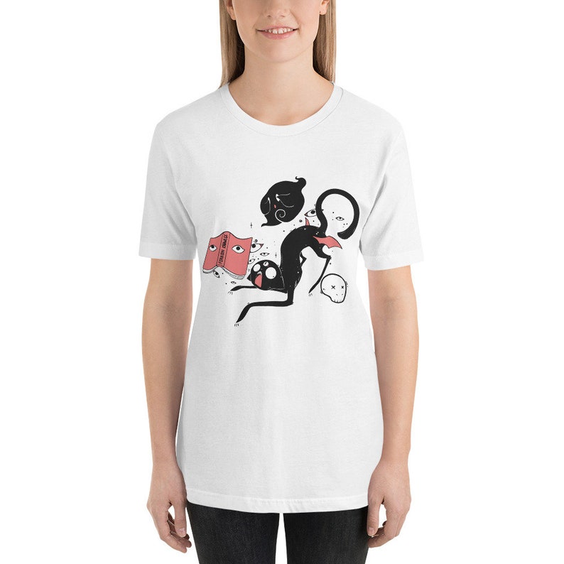 May include: White t-shirt with a black cat illustration wearing a red book on its head. The cat is surrounded by floating eyes and a ghost. The book says "Good Vibes Only".