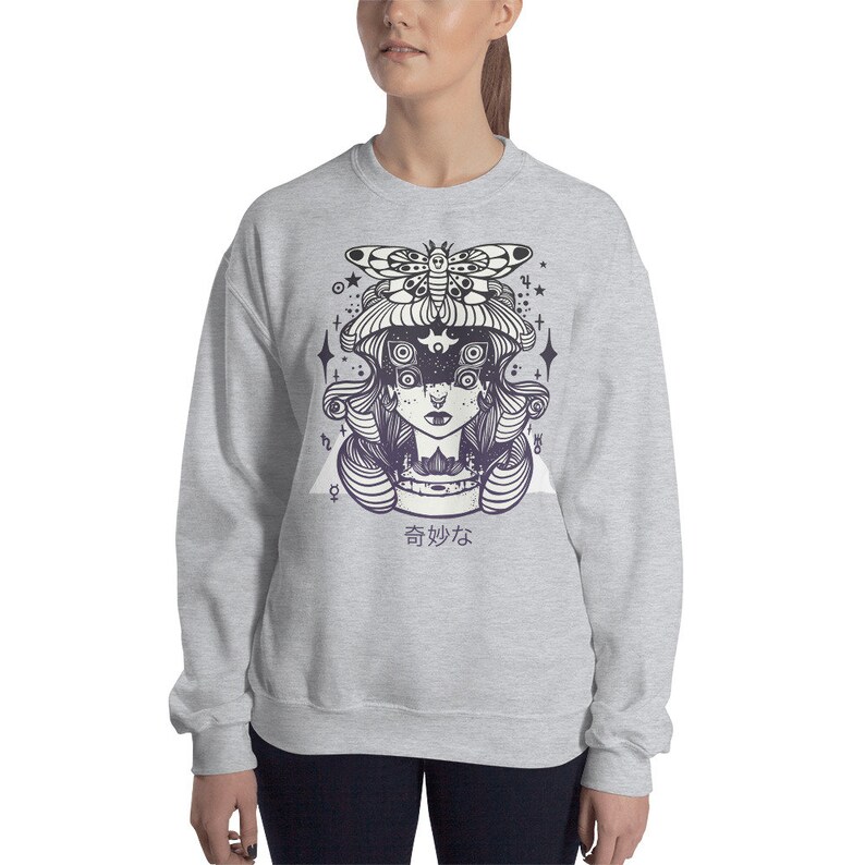 May include: A gray sweatshirt with a graphic print of a woman with a butterfly on her head. The woman has multiple eyes and is surrounded by stars. The text "奇妙な" is printed below the graphic.