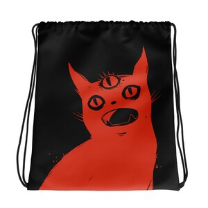 May include: A black drawstring bag featuring a red illustration of a cat with three eyes. The cat has its mouth open wide and is looking upwards.
