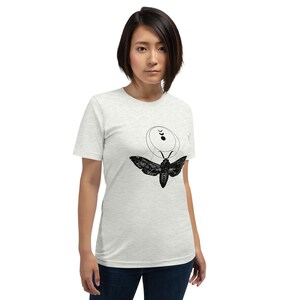 May include: A white t-shirt with a black and white graphic of a moth with a moon and stars design.