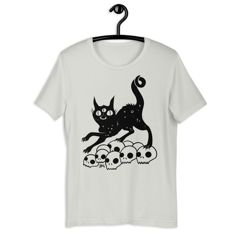 以下が含まれることがあります： 3つの目を持ち、星形の体をした黒い猫が、白い頭蓋骨の山の上に立っています。猫は口を開けて前を向いています。猫は黒で縁取られ、頭蓋骨は黒で塗りつぶされています。