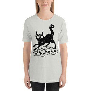 以下が含まれることがあります： 3つの目をした猫が頭蓋骨の山の上に立っている白黒のイラスト。猫の体には星形の模様があります。