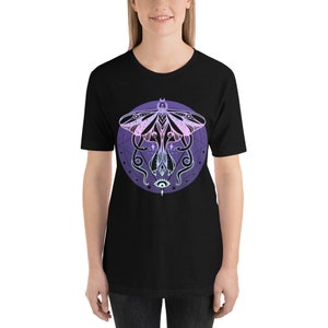 May include: Black t-shirt with a graphic of a moth with a pink and purple gradient, surrounded by a circle with a geometric design and an eye in the center.