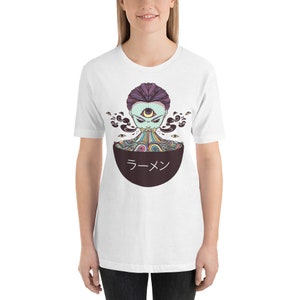 Peut inclure: T-shirt blanc avec un motif d'une cr&eacute;ature psych&eacute;d&eacute;lique color&eacute;e avec un troisi&egrave;me &oelig;il, mangeant des nouilles ramen dans un bol qui dit "ラーメン" en japonais.